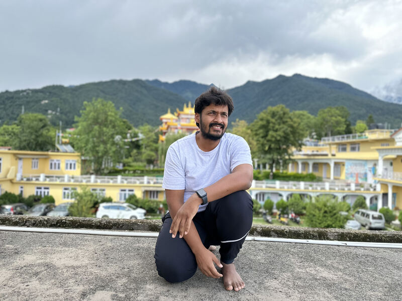Aditya Jain, crouching on a rooftop with hills behind him.