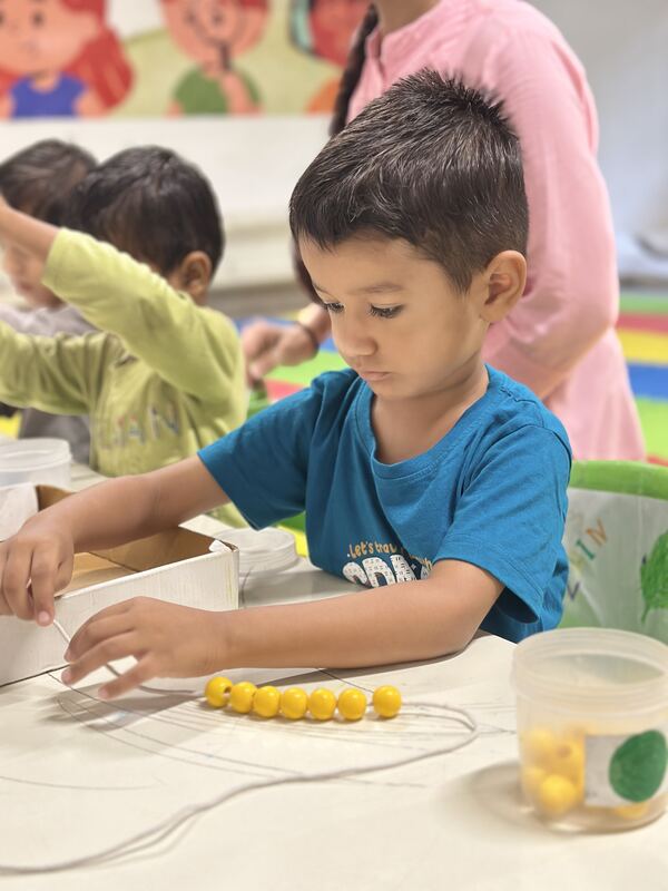A child threading yellow beads onto a wire.