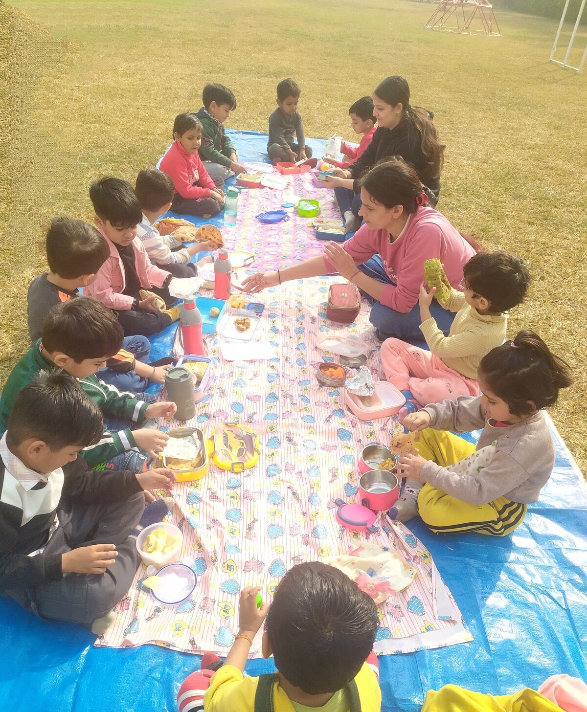 Children eating together on mats spread on the grass outdoors.
