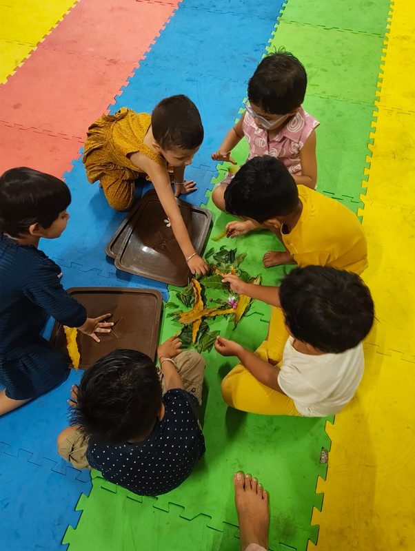 Children on the mat arranging leaves on trays.