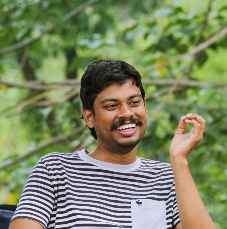 Naveen Vasudevan laughing, in a striped shirt, under the trees.
