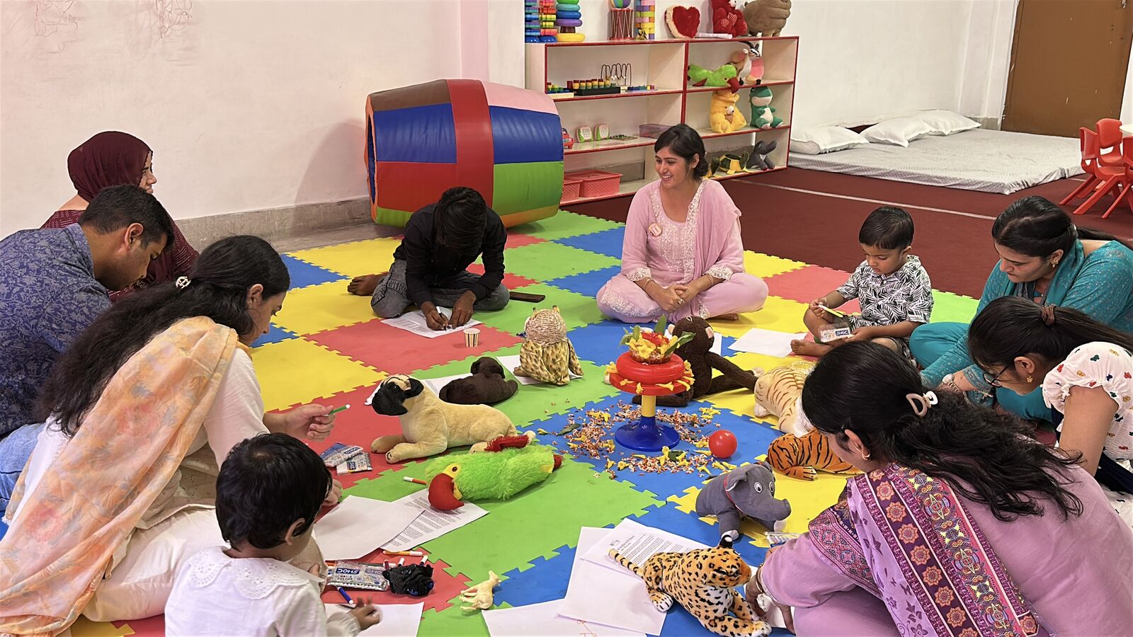 A facilitator sitting on the classroom mat with parents and children around her, at a meeting of the Red group.