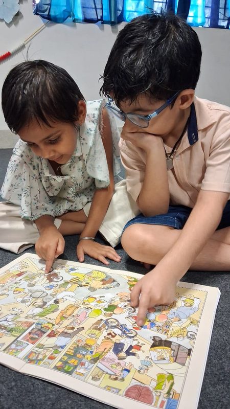 Two children bent over a large picture book on the mat.