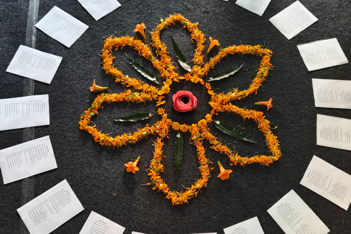 A flower made of marigold petals and leaves on a dark cloth, ringed by printed pages.
