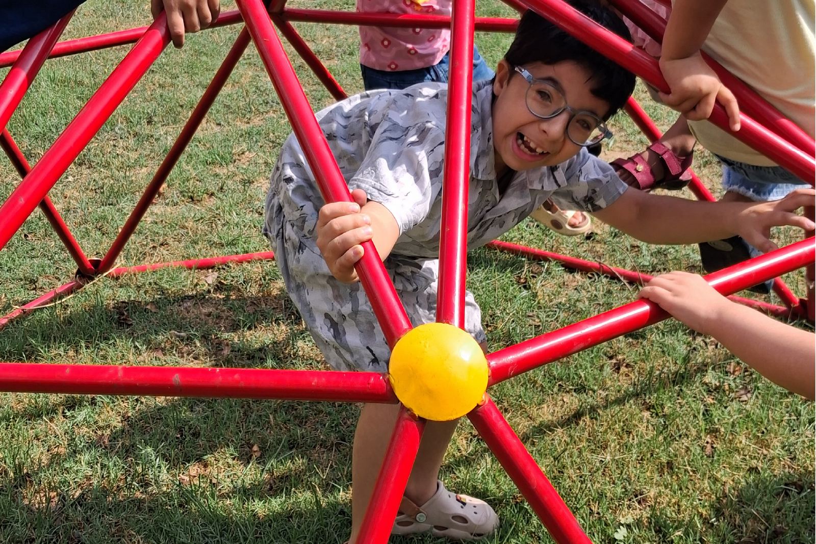 A child climbing through the red bars of the climbing dome on the grass.