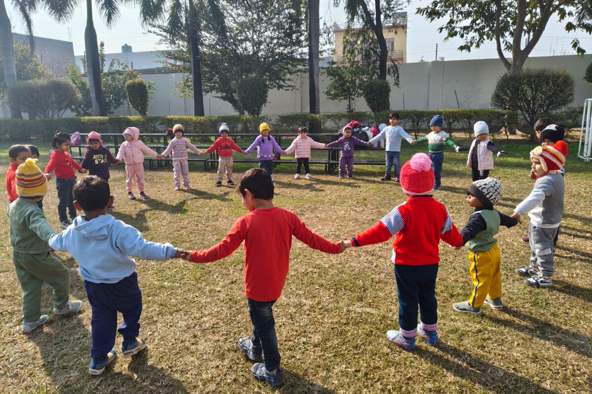 Children holding hands in a wide circle on the college lawn.
