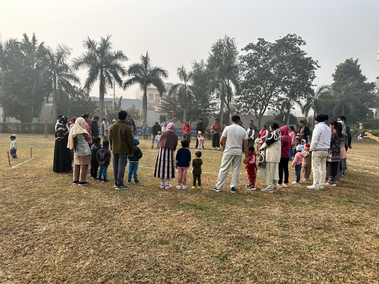 Children and parents in a loose circle on the college ground on a foggy winter morning, palm trees fading into the fog.