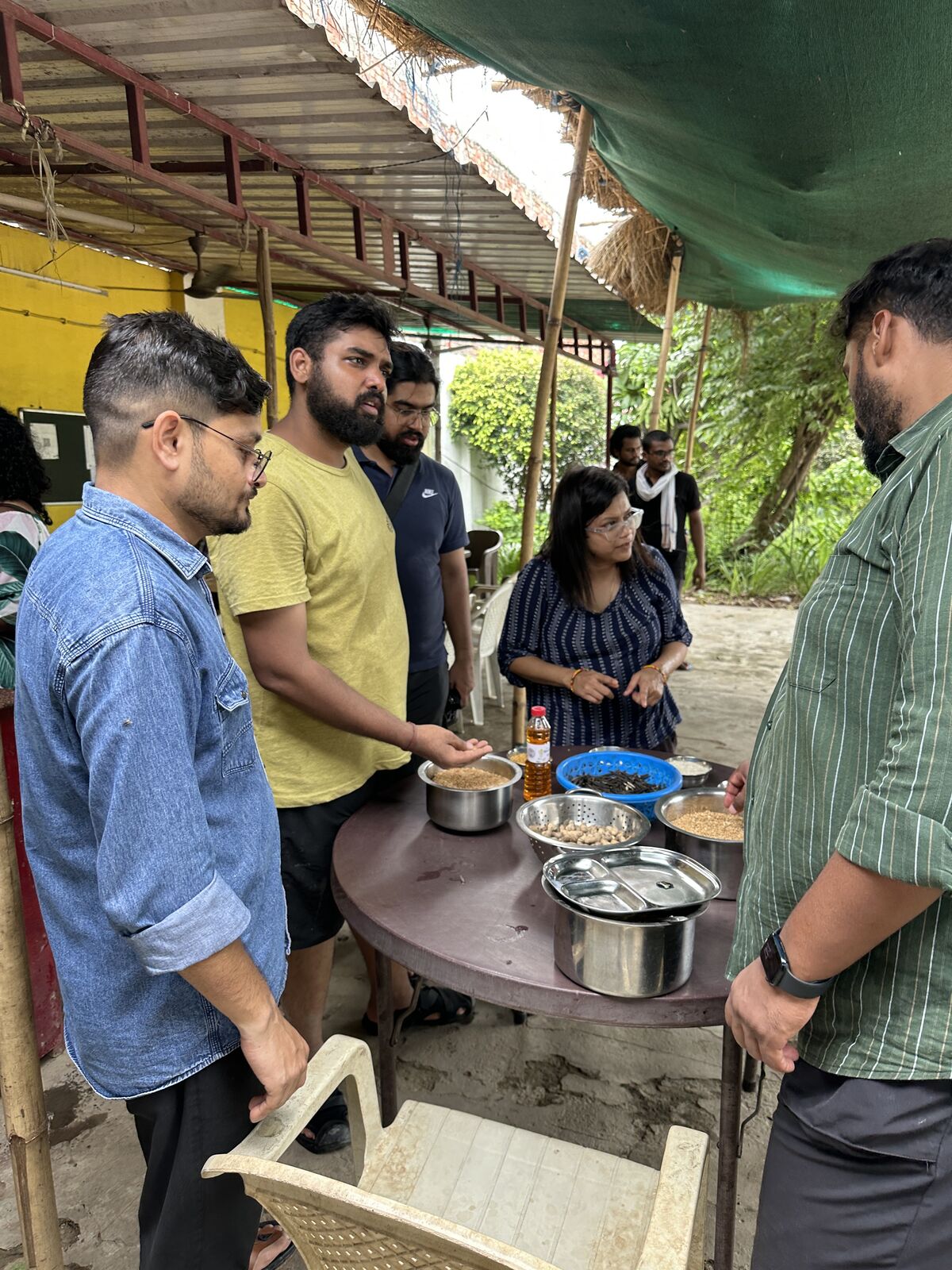 The team cooking together under a shade outdoors, pots on the stove, one person stirring.