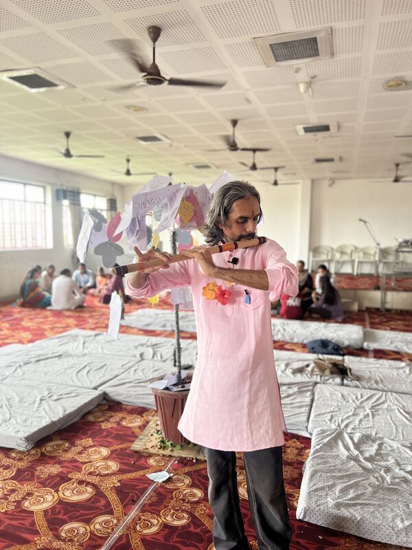 Vaibhav, in a pink kurta, holding up a paper craft in the hall.
